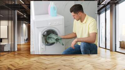 Man putting clothes into washing machine in bathroom. Laundry day Wall mural