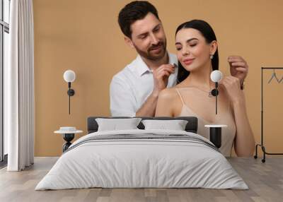 Man putting elegant necklace on beautiful woman against beige background Wall mural