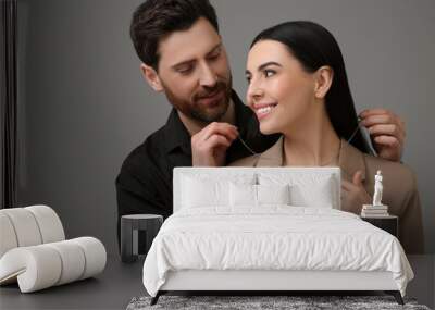 Man putting elegant necklace on beautiful woman against dark grey background Wall mural