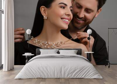 Man putting elegant necklace on beautiful woman against grey background, closeup Wall mural