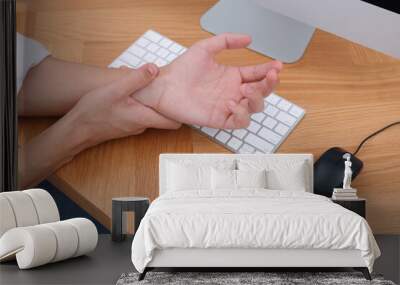 Man suffering from pain in wrist while working on computer at table indoors, closeup. Carpal tunnel syndrome Wall mural