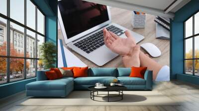 Man suffering from pain in wrist while working on laptop at table indoors, closeup. Carpal tunnel syndrome Wall mural