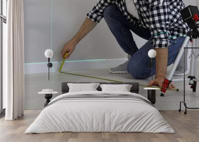 Man using cross line laser level and tape for accurate measurement on floor, closeup Wall mural