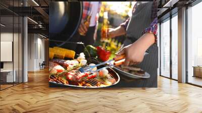 Man with drink cooking meat and vegetables on barbecue grill outdoors, closeup Wall mural