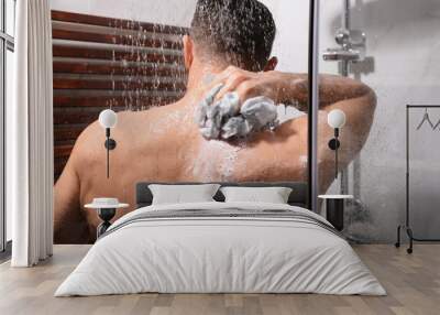 Man with mesh pouf taking shower at home, back view Wall mural