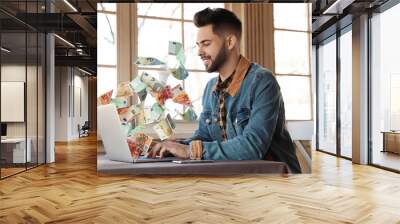 Man with modern laptop and flying euro banknotes at table indoors. People make money online Wall mural