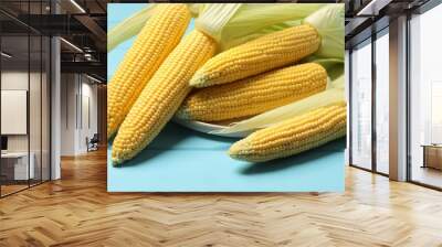 Many fresh ripe corncobs with green husks on light blue wooden table Wall mural