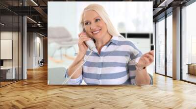 Mature woman talking on phone at workplace Wall mural