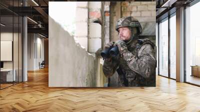 Military mission. Soldier in uniform with binoculars inside abandoned building, space for text Wall mural