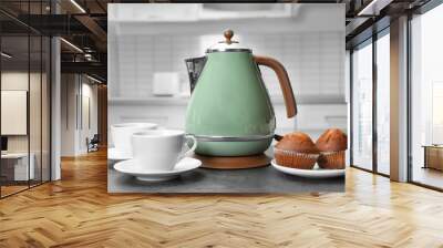 Modern electric kettle, cups and muffins on grey table in kitchen Wall mural