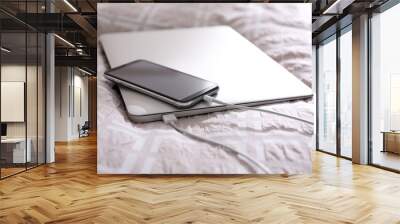 Modern laptop and mobile phone with chargers on bed, closeup Wall mural