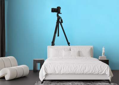 Modern tripod with professional camera on light blue background Wall mural