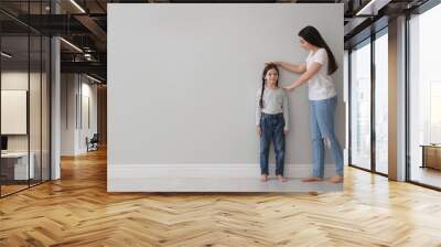 Mother measuring little girl's height near light grey wall indoors. Space for text Wall mural