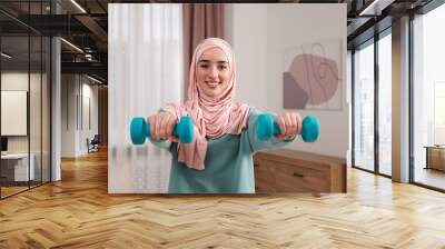 Muslim woman in hijab doing exercise with dumbbells at home Wall mural