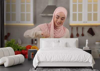 Muslim woman making delicious salad with vegetables at white table in kitchen Wall mural