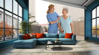 Nurse assisting elderly woman with cane indoors Wall mural