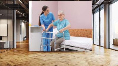 Nurse assisting senior woman with walker to get up from bed in hospital ward Wall mural