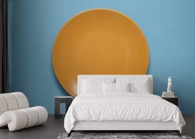 One orange ceramic plate on light blue background, top view Wall mural