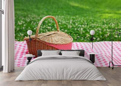 One picnic wicker basket with checkered napkin and blanket on green grass. Space for text Wall mural