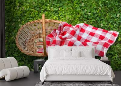 One picnic wicker basket with checkered napkin on green grass, above view Wall mural