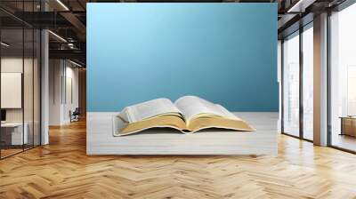 Open Bible on white wooden table against turquoise background. Christian religious book Wall mural