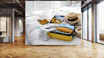 Open suitcase full of clothes, shoes and summer accessories on bed Wall mural