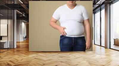 Overweight man in tight t-shirt on beige background, closeup. Space for text Wall mural