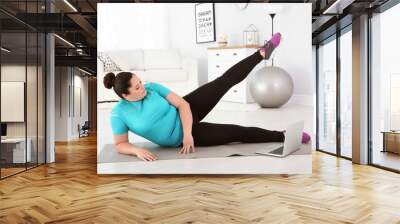 Overweight woman doing exercise while watching tutorial on laptop at home Wall mural