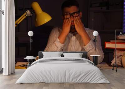 Overwhelmed man at workplace in office at night Wall mural