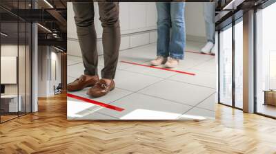 People standing in line behind taped floor markings for social distance indoors, closeup. Coronavirus pandemic Wall mural