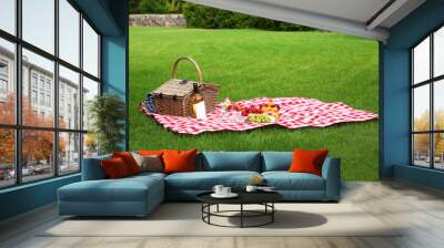 Picnic basket with products and bottle of wine on checkered blanket in garden Wall mural