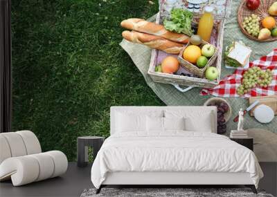 Picnic wicker basket with delicious food and drink on blanket outdoors, above view. Space for text Wall mural