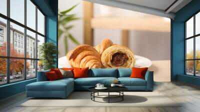 Plate of fresh croissants with chocolate stuffing on wooden table indoors. French pastry Wall mural