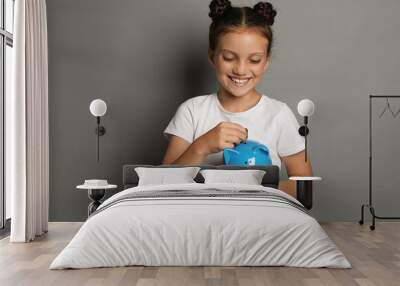 Pocket money. Cute girl putting coins into piggy bank on grey background Wall mural