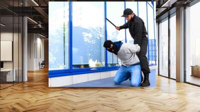 Police officer with baton arresting masked criminal outdoors Wall mural