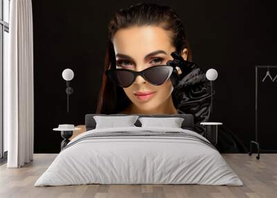 Portrait of beautiful young woman in sunglasses and elegant evening gloves on black background Wall mural