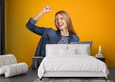 Portrait of emotional woman with modern laptop on yellow background Wall mural