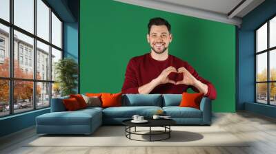 Portrait of handsome man making heart with his hands on color background Wall mural