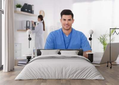 Portrait of male doctor at table in modern clinic Wall mural