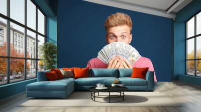 Portrait of surprised lottery winner with money fan on blue background Wall mural