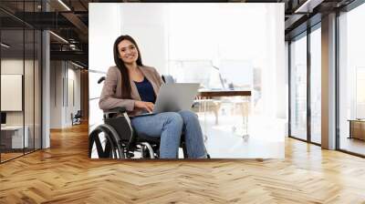 Portrait of young woman in wheelchair with laptop at office Wall mural