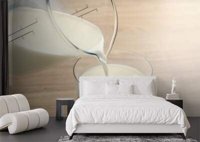 Pouring fresh milk from jug into glass at wooden table, closeup Wall mural