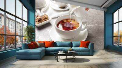 Pouring milk into cup of black tea on table Wall mural