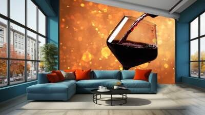 Pouring red wine into glass against orange background with blurred lights, closeup. Space for text Wall mural