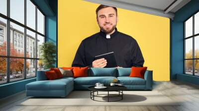 Priest in cassock with Bible on yellow background Wall mural