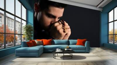 Priest with rosary beads praying on black background, closeup. Space for text Wall mural