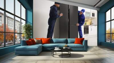 Professional workers carrying modern refrigerator in kitchen Wall mural