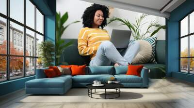 Relaxing atmosphere. Happy woman with laptop on sofa near beautiful houseplants in room Wall mural