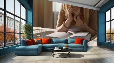 Religious young woman praying over Bible in bedroom Wall mural