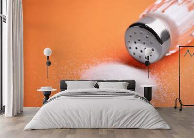 Scattered salt and shaker on orange background, closeup. Space for text Wall mural